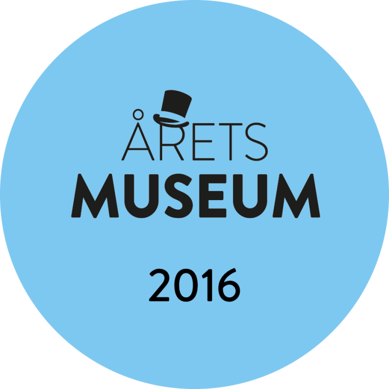 Blue round badge showing MUSEUM OF THE YEAR 2016 in black text, with an illustration of a top hat above the letter A in ARETS, symbolizing a prestigious museum award.