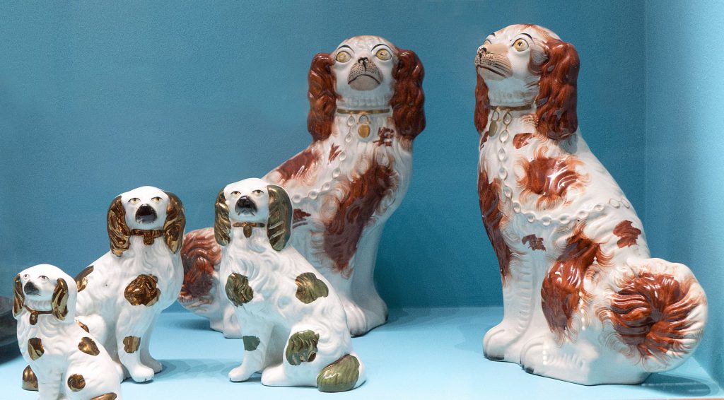 Fem keramiska spanielhundfigurer med vita kroppar och bruna eller guldfärgade teckningar visas mot en ljusblå bakgrund, vilket blir ett charmigt tillskott till vilket kuriosakabinett som helst.