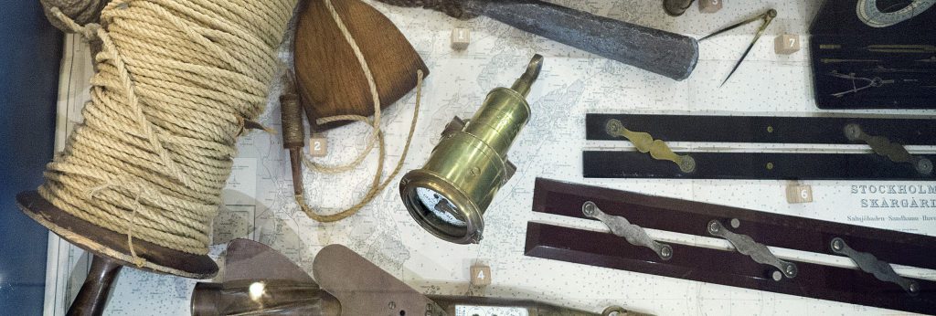 En monter med navigationsverktyg och utrustning, inklusive en reprulle, trä- och metallinstrument, en mässingskompass och kartfragment.