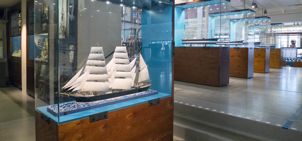 Ett modellsegelfartyg utställt i en glasmontre på ett sjöfartsmuseum, bland andra imponerande skeppsmodeller i Utställningarna.