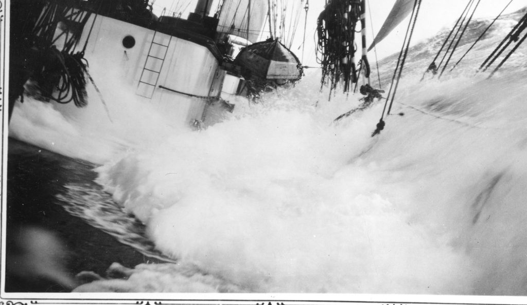 A large wave crashes over the deck of a sailing vessel, capsizing the ship and splashing water among ropes and equipment – ​​a dramatic reminder of the importance of maritime safety at sea.