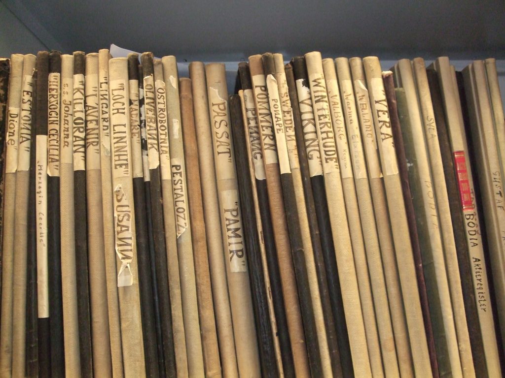 A shelf filled with scrolled documents or maps, each labeled with handwritten names and titles on the spine for identification.